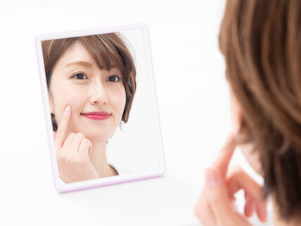 頬を触りながら鏡を見る女性